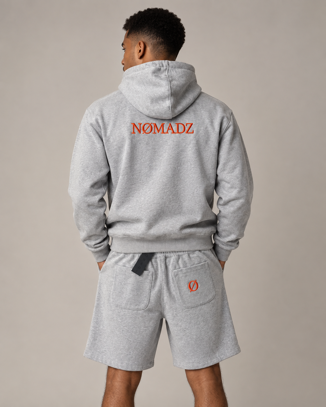 NØMADZ grey hoodie and men's shorts set with orange logo on the back worn by a model