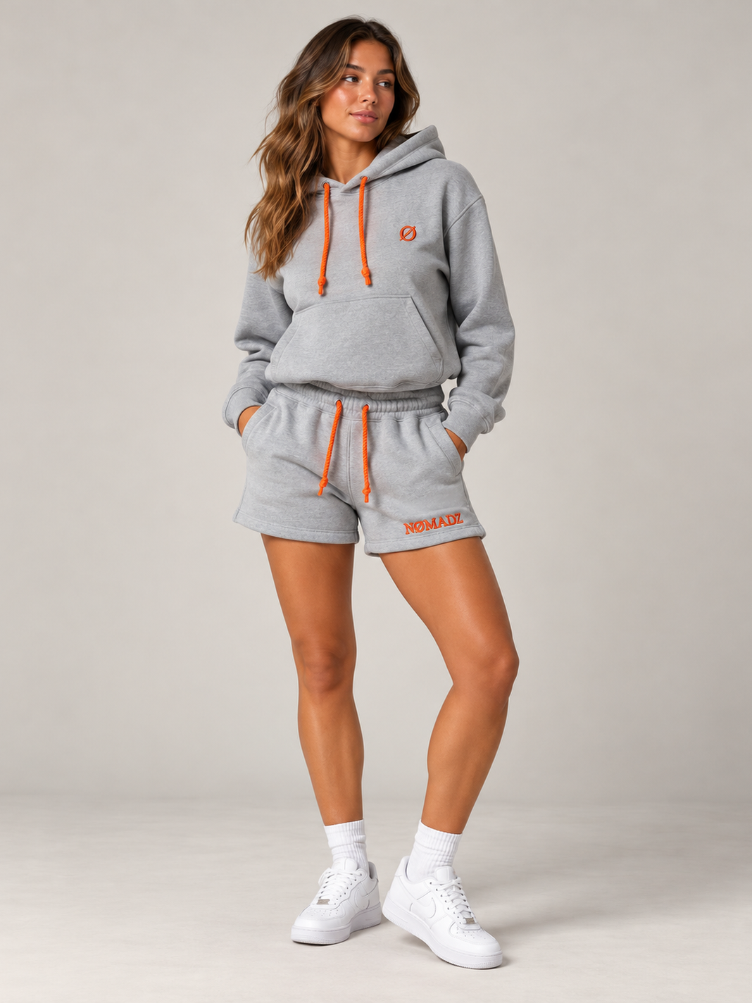 NØMADZ grey hoodie and women's shorts set with terracotta orange embroidery worn by a model